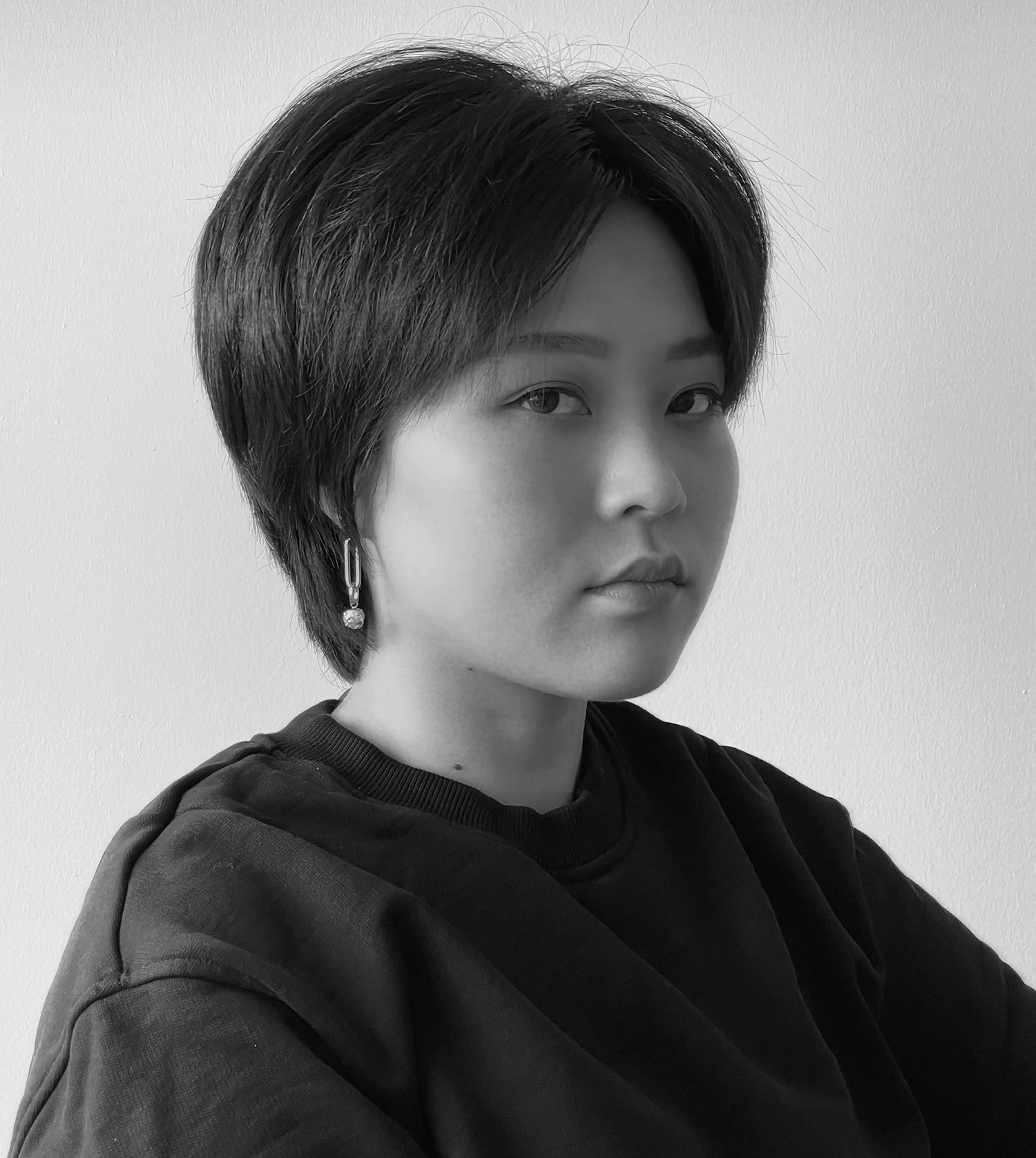 Black & white picture of a young Asian woman with short hair wearing earings and a pullover, looking directly at the camera.